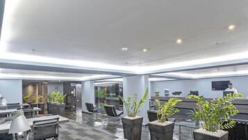 A modern hotel lobby with a reception desk, seating area, and potted plants.