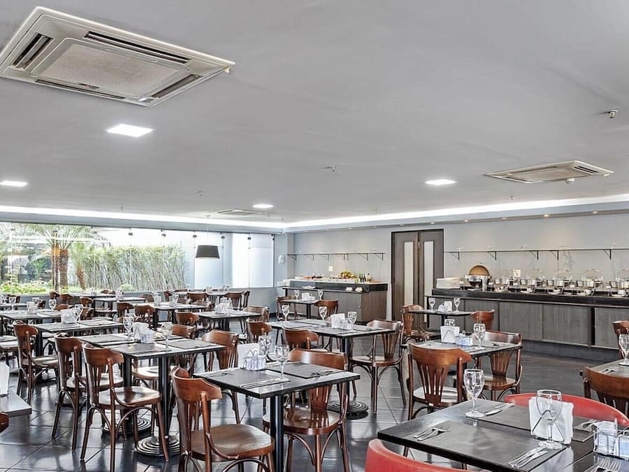 A spacious restaurant with multiple tables and chairs, a kitchen area, and large windows allowing natural light.