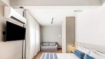 Een moderne hotelkamer met een flatscreen televisie aan de muur, een sofa, een bed met kussens en een nachtkastje met een lamp.