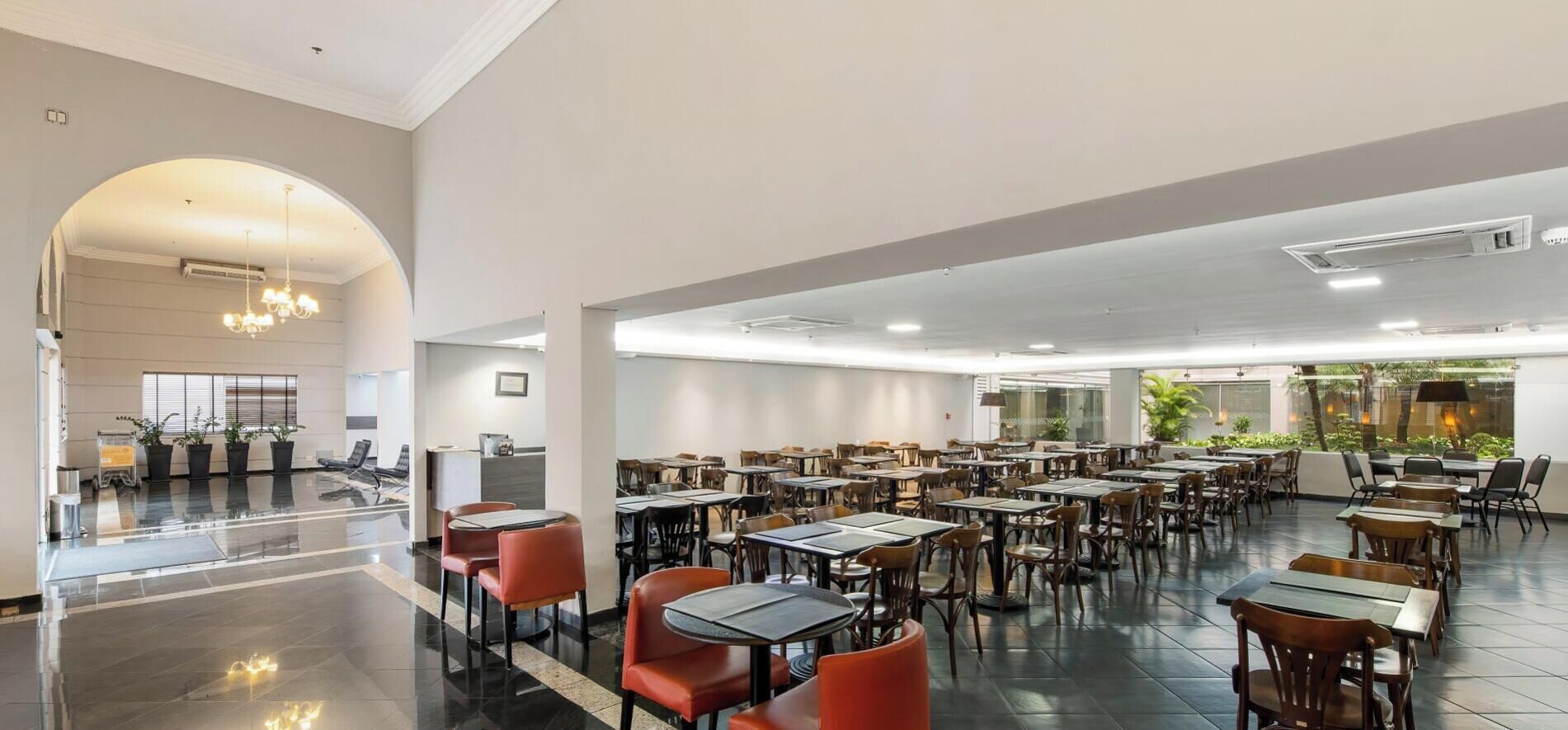 Un vaste espace de restauration intérieur, doté de nombreuses tables et chaises, d’un comptoir d’accueil central et d’une grande porte en arc de cercle.