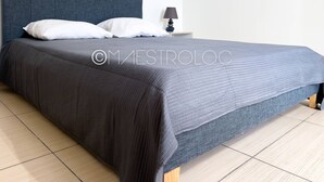 A neatly made bed with a dark grey headboard and matching grey bedding. - Villa Exotique (Le Moule)