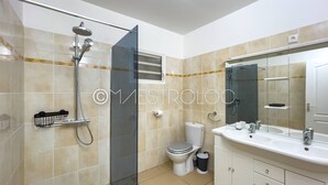 A modern bathroom with a glass shower enclosure, a toilet, a sink with a mirror, and a cabinet with drawers. - Villa Exotique (Le Moule)