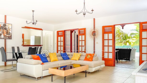 A modern living room with a sofa, coffee table, and dining area. - Villa Exotique (Le Moule)