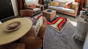 A cozy living room with a sofa set, a dining table, and a large window with curtains. - Bright Boho Walkable House Bars Beaches Bike Path Downtown (Muskegon)