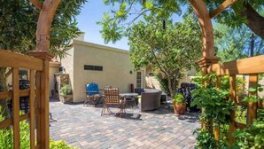 An outdoor patio area with a stone floor, wooden pergola, and outdoor furniture. - Garden Patio Home in Chandler, AZ (Chandler)