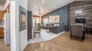 A spacious living room with a gray sofa, a dining area with a table and chairs, and a kitchen with a refrigerator. - Garden Patio Home in Chandler, AZ (Chandler)
