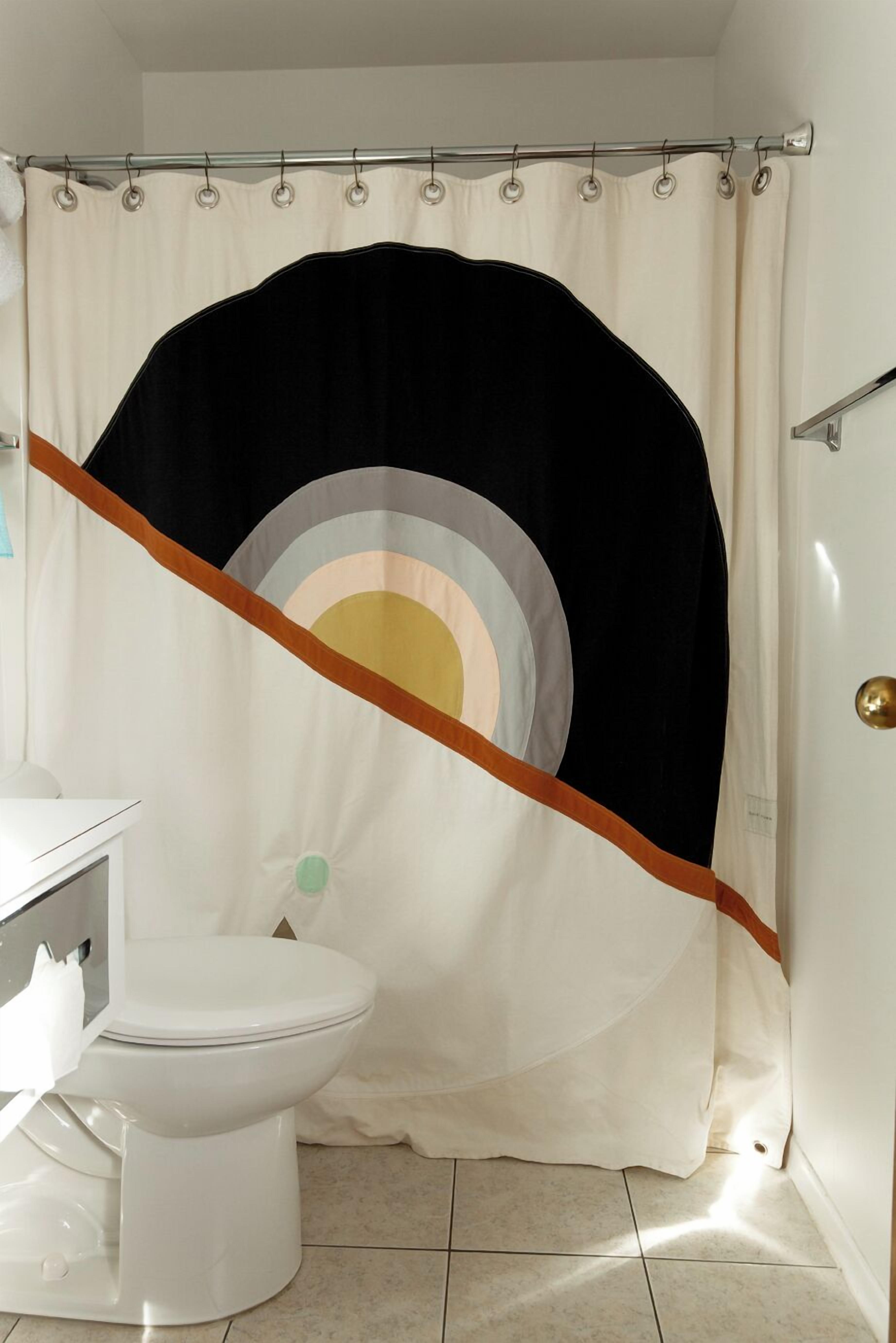 Une salle de bain comprenant des toilettes, un rideau de douche à motifs géométriques et un porte-serviettes.