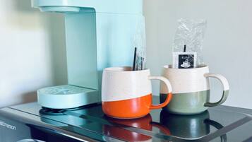 Una cafetera sobre un microondas, con dos tazas encima.