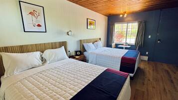 Een hotelkamer met twee bedden, een houten plafond, een raam met gordijnen en een ingelijst schilderij aan de muur.