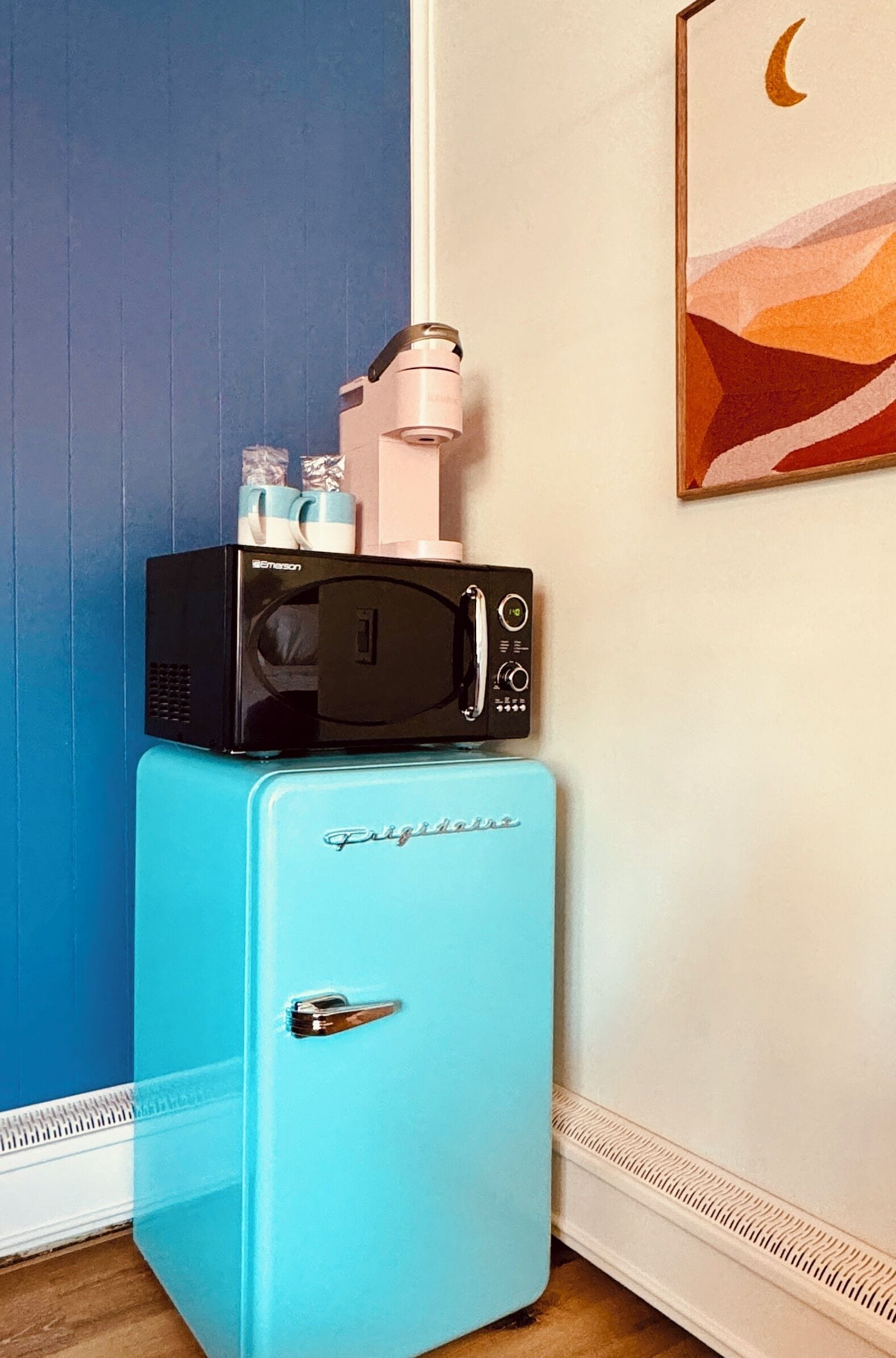 A retro-style refrigerator with a microwave on top, a door handle, and a brand name visible.