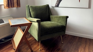 A green armchair, a wooden side table, and a wall-mounted painting of a bird on a branch. - The Sierra Motel (Traverse City)