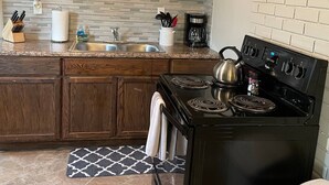 A kitchen with wooden cabinets, a black stove, a sink, and a backsplash with a lemon wreath. - Clean Apartment close to 80/94, I65 Lake Station 2751 DeKalb 1 bed (Lake Station)