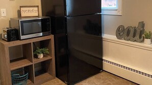 A kitchen with a black refrigerator, a microwave, and a small wooden shelf with a plant. - Clean Apartment close to 80/94, I65 Lake Station 2751 DeKalb 1 bed (Lake Station)