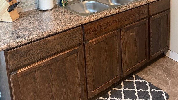 A kitchen with wooden cabinets, a granite countertop, a double sink, and a decorative wall hanging of lemons. - Clean Apartment close to 80/94, I65 Lake Station 2751 DeKalb 1 bed (Lake Station)