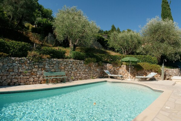 Relax by the serene pool surrounded by lush greenery and a stone wall.