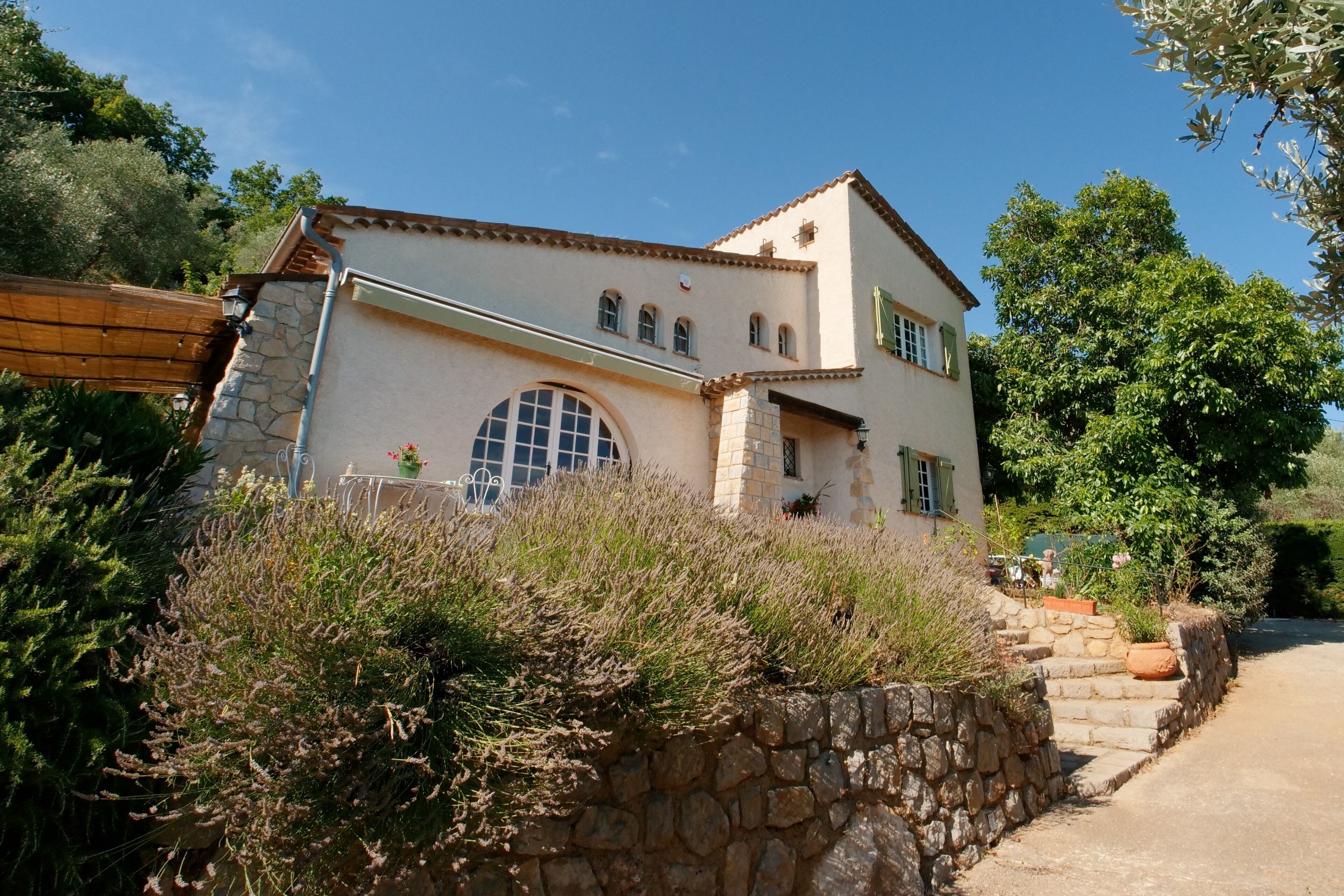 Una casa de dos pisos con fachada de piedra, un amplio ventanal de arco y una escalera de piedra que conduce a la entrada.