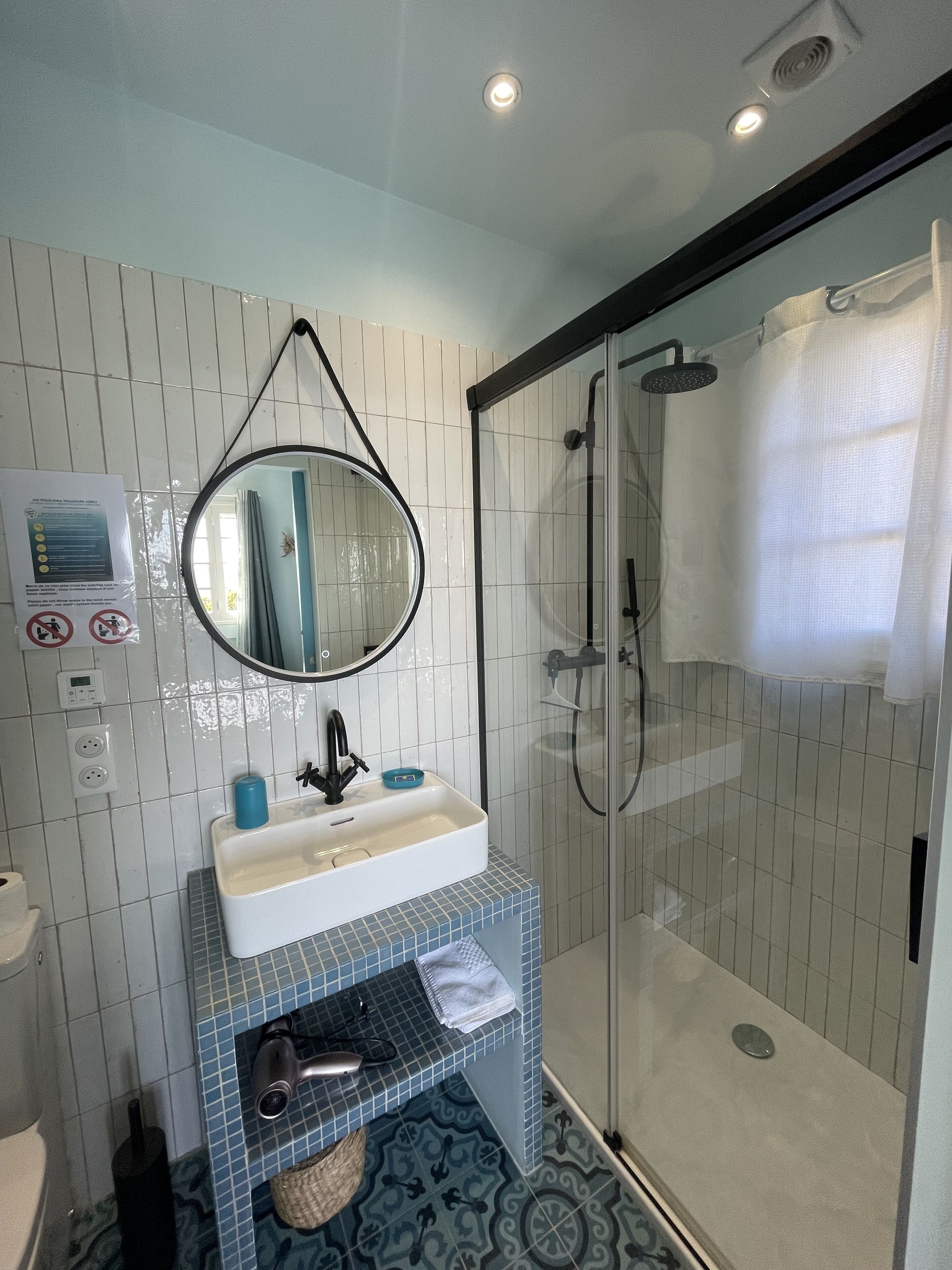Een badkamer met een wit wastafel, een spiegel, een douche en een betegelde vloer.