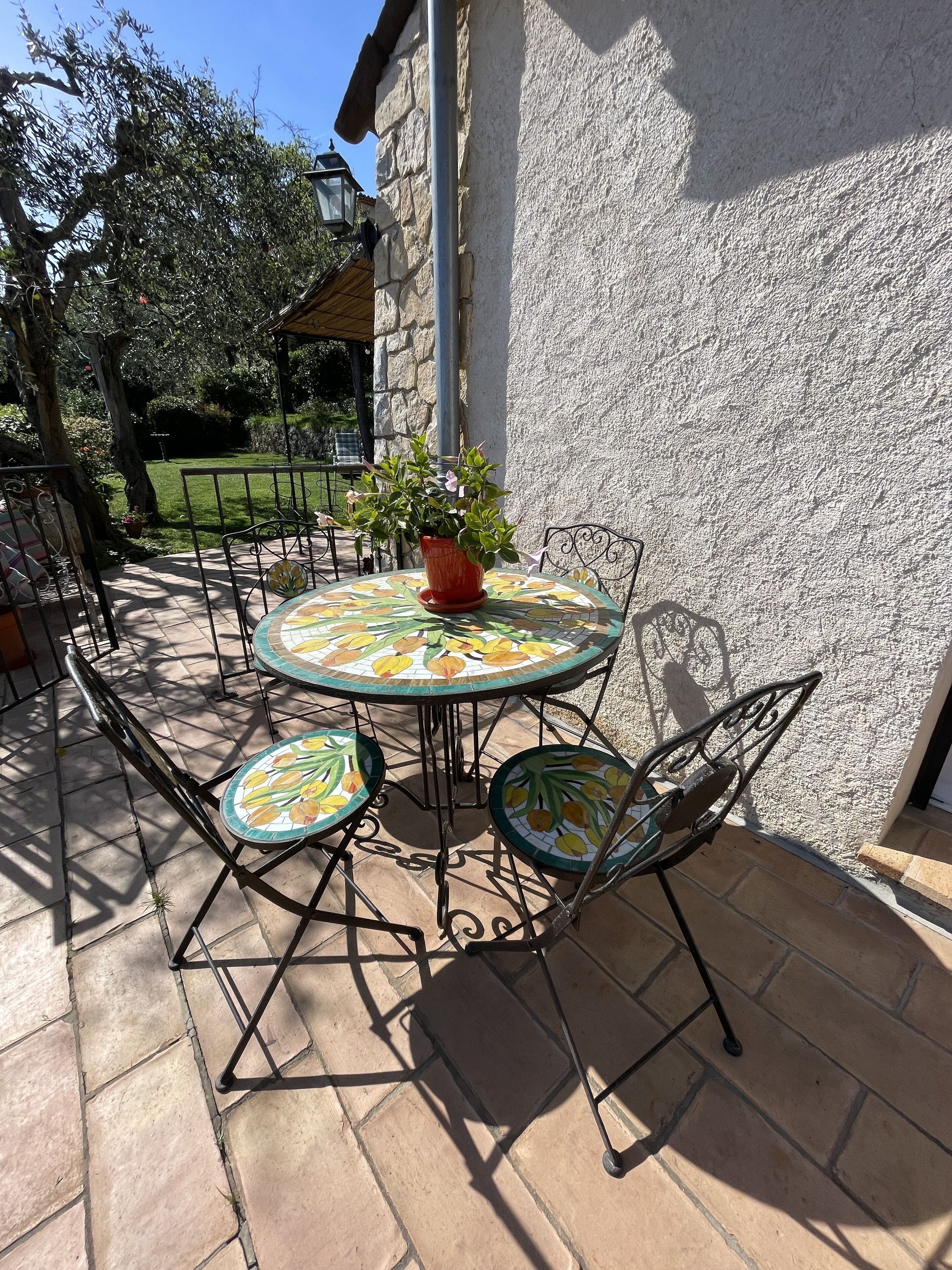 Een terras buiten met een ronde tafel en vier stoelen, omringd door stenen tegels.