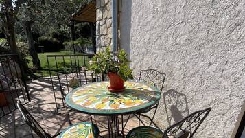Een terras buiten met een ronde tafel en vier stoelen, omringd door stenen tegels.