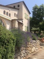 Un edificio de piedra de dos plantas con techo inclinado, contraventanas verdes y una escalera de piedra que lleva a la entrada.