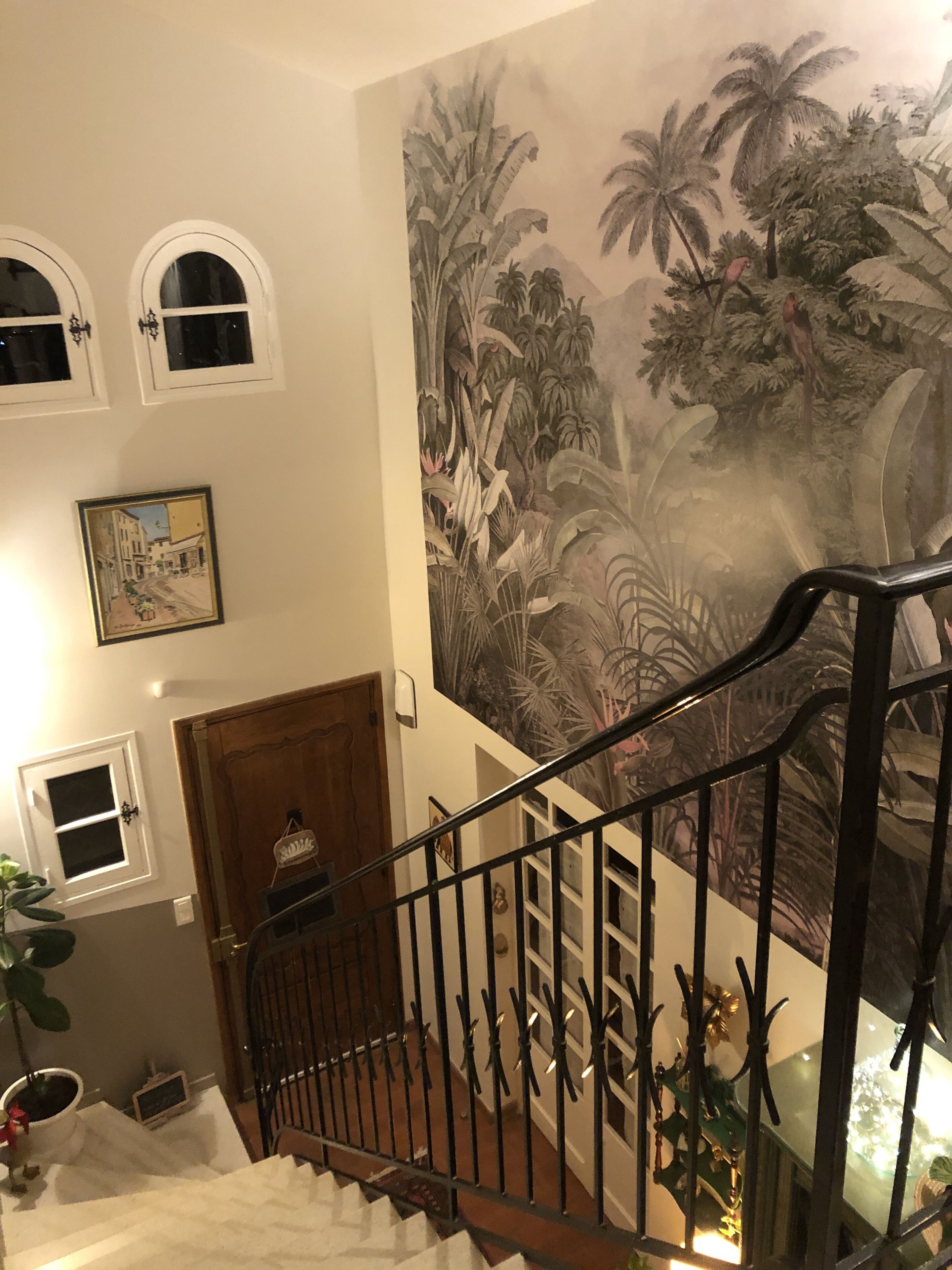 Eine Treppe mit Wandgemälde von tropischem Grünwerk, einer Holztür und einem gerahmten Bild an der Wand.