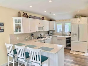 Una cocina moderna con armarios blancos, una isla central con sillas, una estufa y un refrigerador.