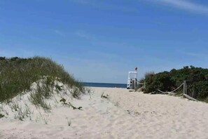 Una playa arenosa con dunas y una torre de salvavidas a lo lejos.