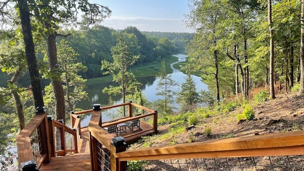 A wooden deck with a railing overlooking a river and forested area.