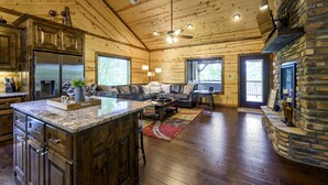 A spacious living area with a large wooden ceiling, a stone fireplace, and a modern kitchen with stainless steel appliances.