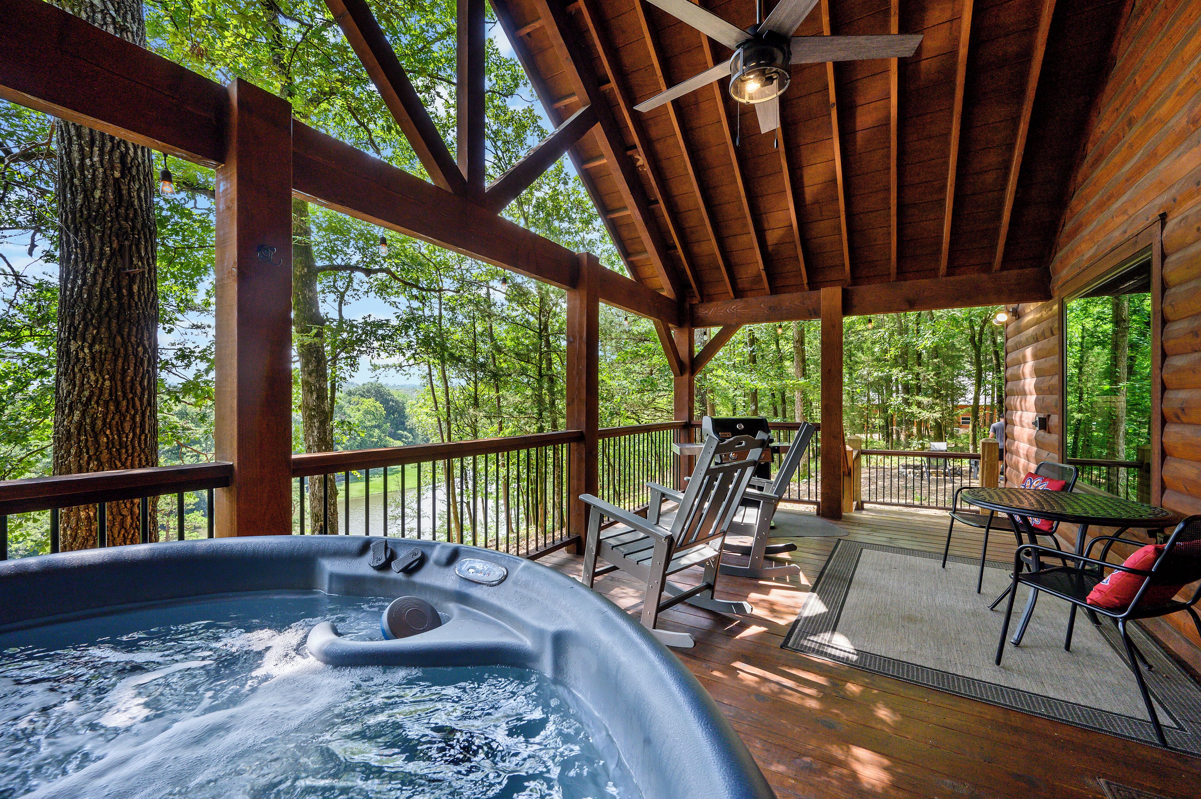 A hot tub on a wooden deck with a view of trees and a wooden cabin in the background.