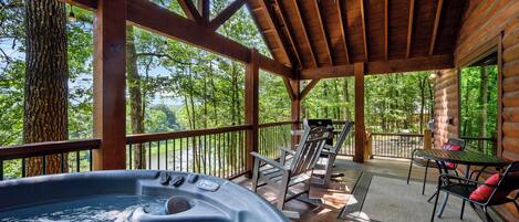 A hot tub on a wooden deck with a view of trees and a wooden cabin in the background.