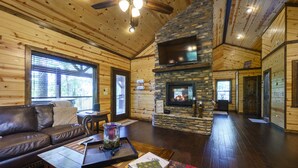 A cozy cabin interior with a stone fireplace, wooden walls, a leather sofa, and a dining area.