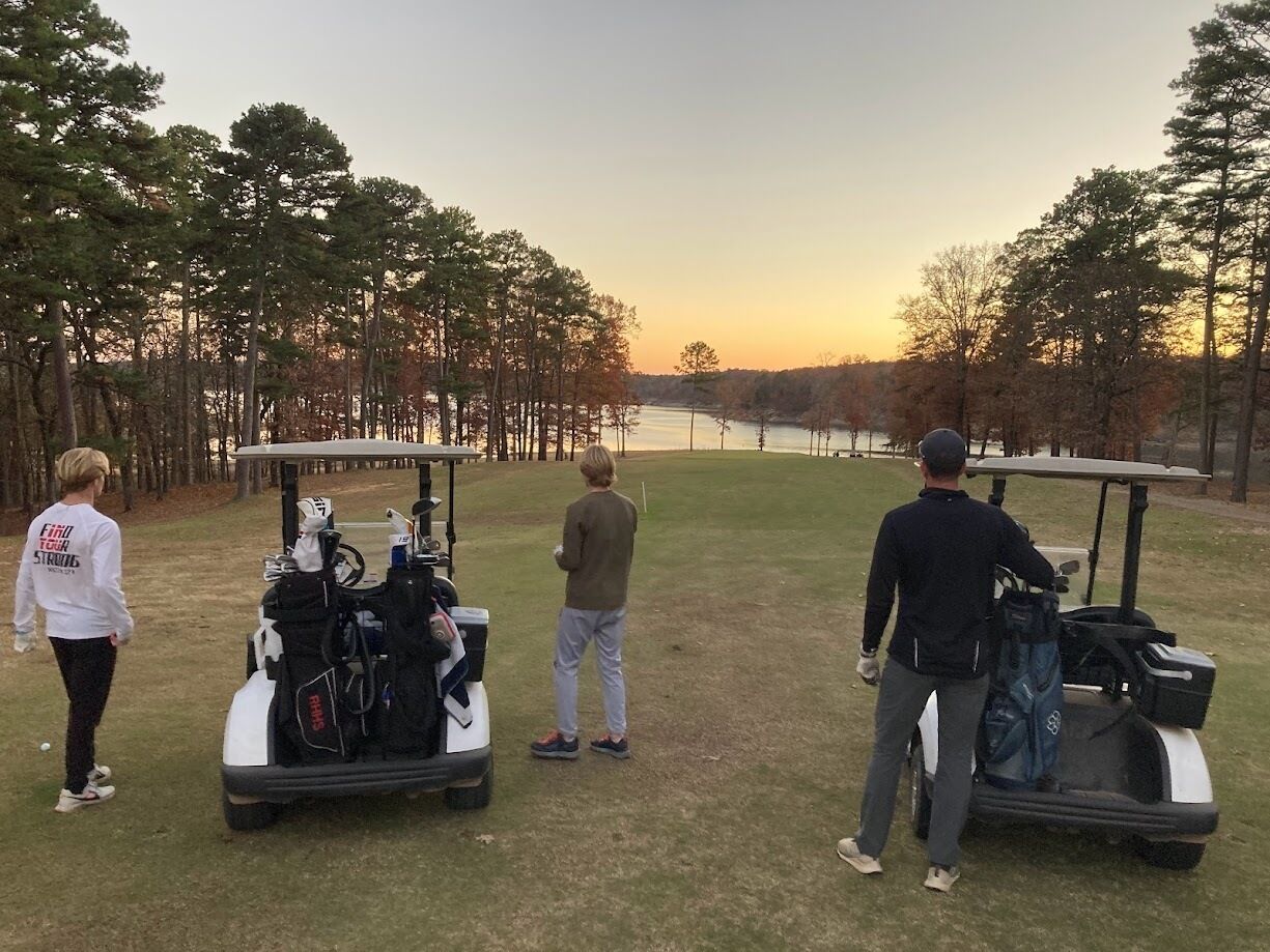 A golf course with three golf carts and players.