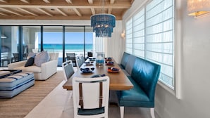 A dining area with a wooden table, blue upholstered bench, and a view of the ocean.