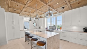 A spacious kitchen with a large island, bar stools, and a wooden ceiling.