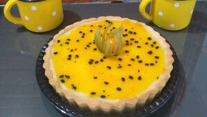 A pie on a black plate with a yellow crust and black specks, placed on a table with two yellow mugs with white polka dots. - Hotel Metropolitano  (Major Vieira)