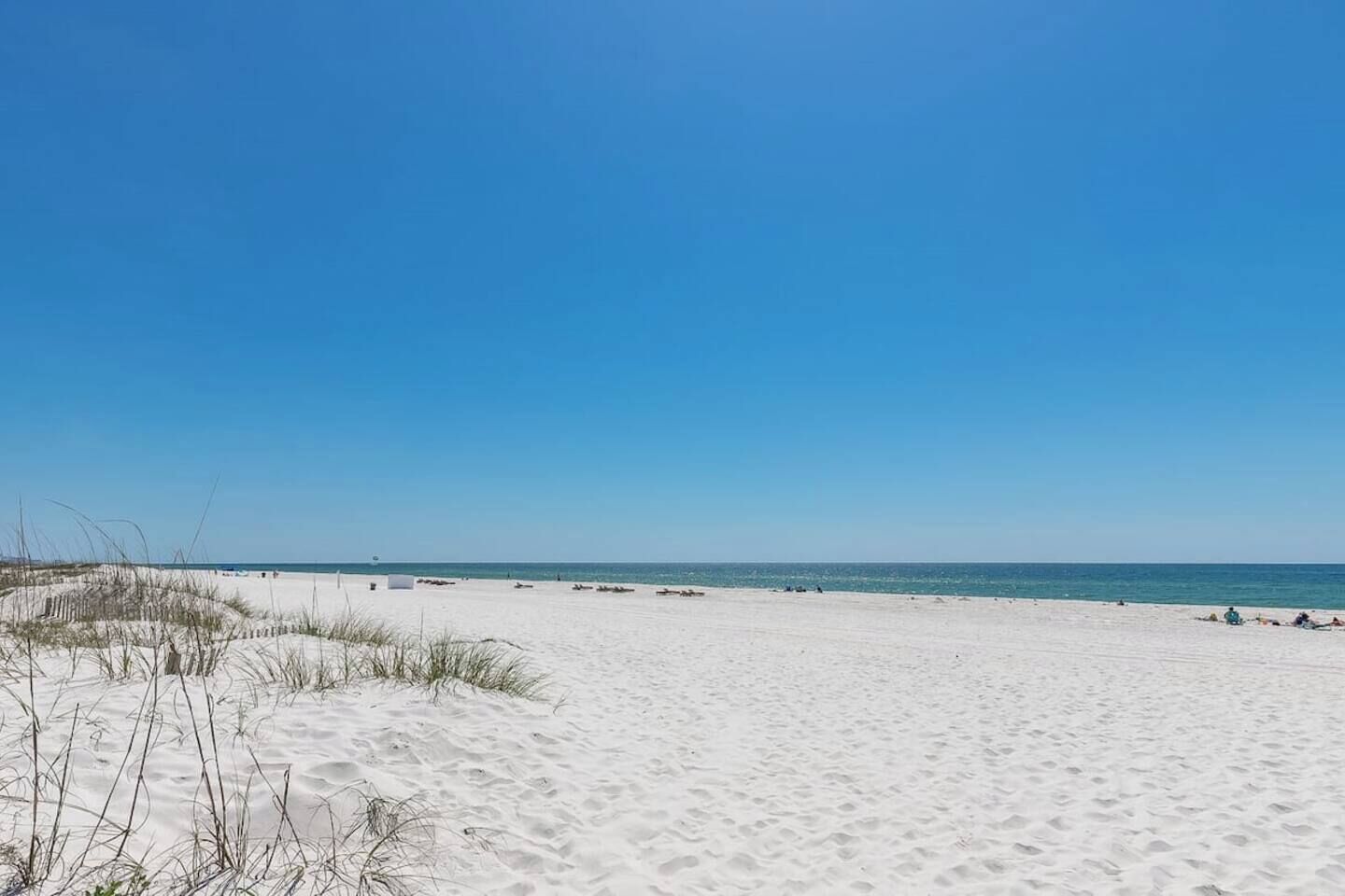 Een zandstrand met duinen en een helderblauwe lucht.