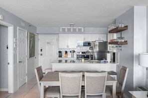 A modern kitchen with white cabinetry, a central island, and a dining area with four chairs.