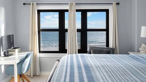 Une chambre d’hôtel avec un lit, un bureau équipé d’un ordinateur, une chaise et une vue sur la mer grâce à de grandes fenêtres.