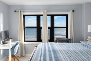 A hotel room with a bed, a desk with a computer, a chair, and a view of the sea through large windows. - Stunning Beach View! Heated Pools! Family Friendly (Orange Beach)