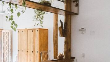 Une chambre à coucher avec un lit, un bureau en bois, une plante suspendue, et une vue sur une armoire en bois et une chaise.