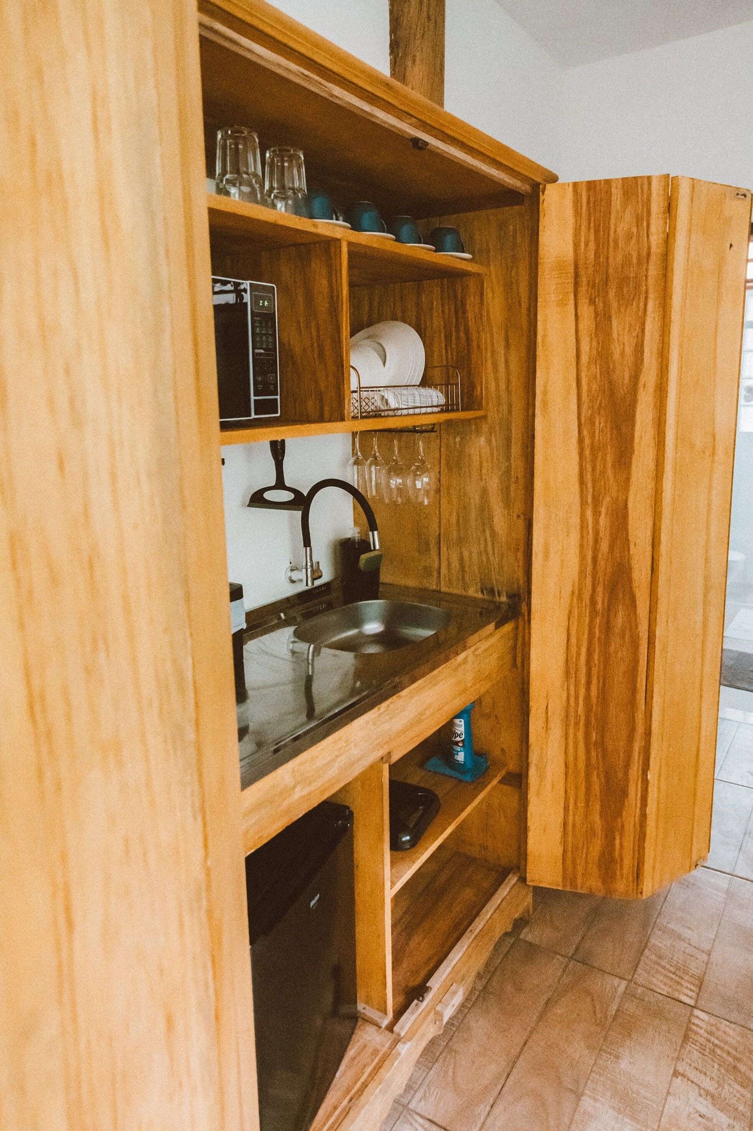 Una cucina in legno con lavello integrato, mensole con bicchieri e un forno a microonde.