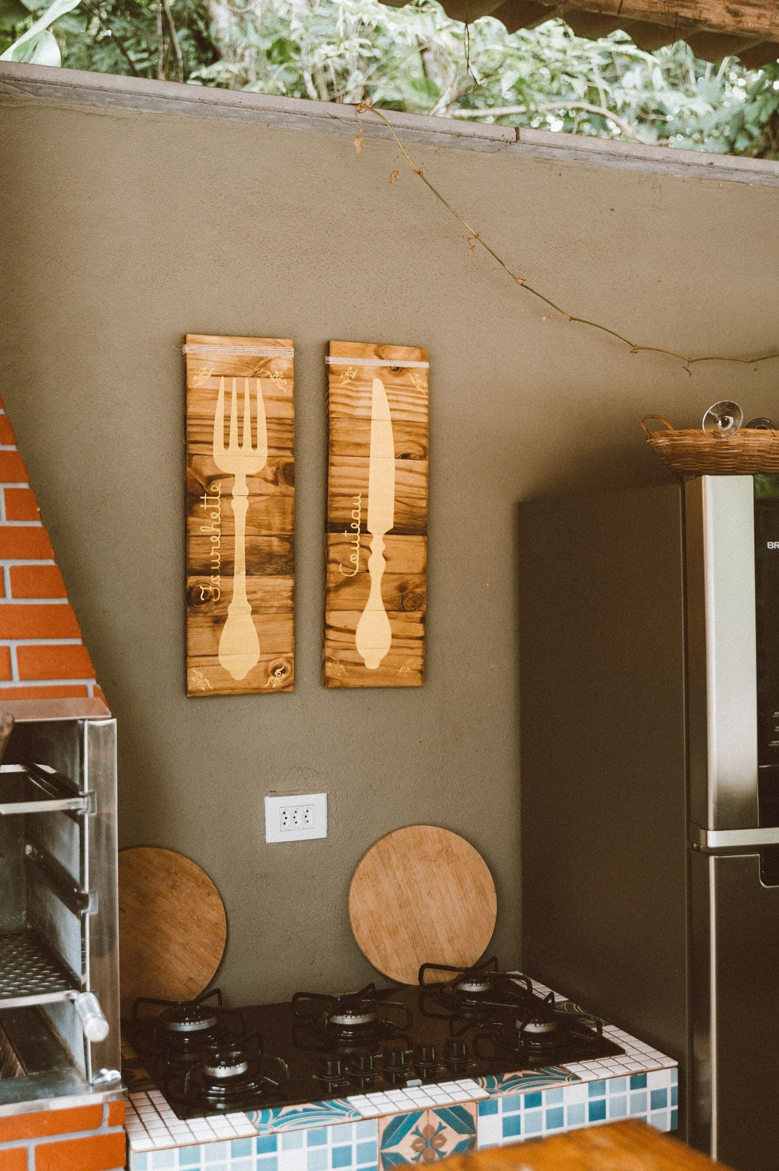Una cocina con estufa a gas, dos adornos de madera en la pared, un horno de ladrillo y un refrigerador.