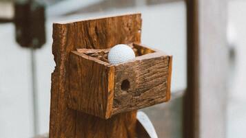 Un tee de madera con una pelota de golf en una caja de madera, sujeto a un soporte metálico.