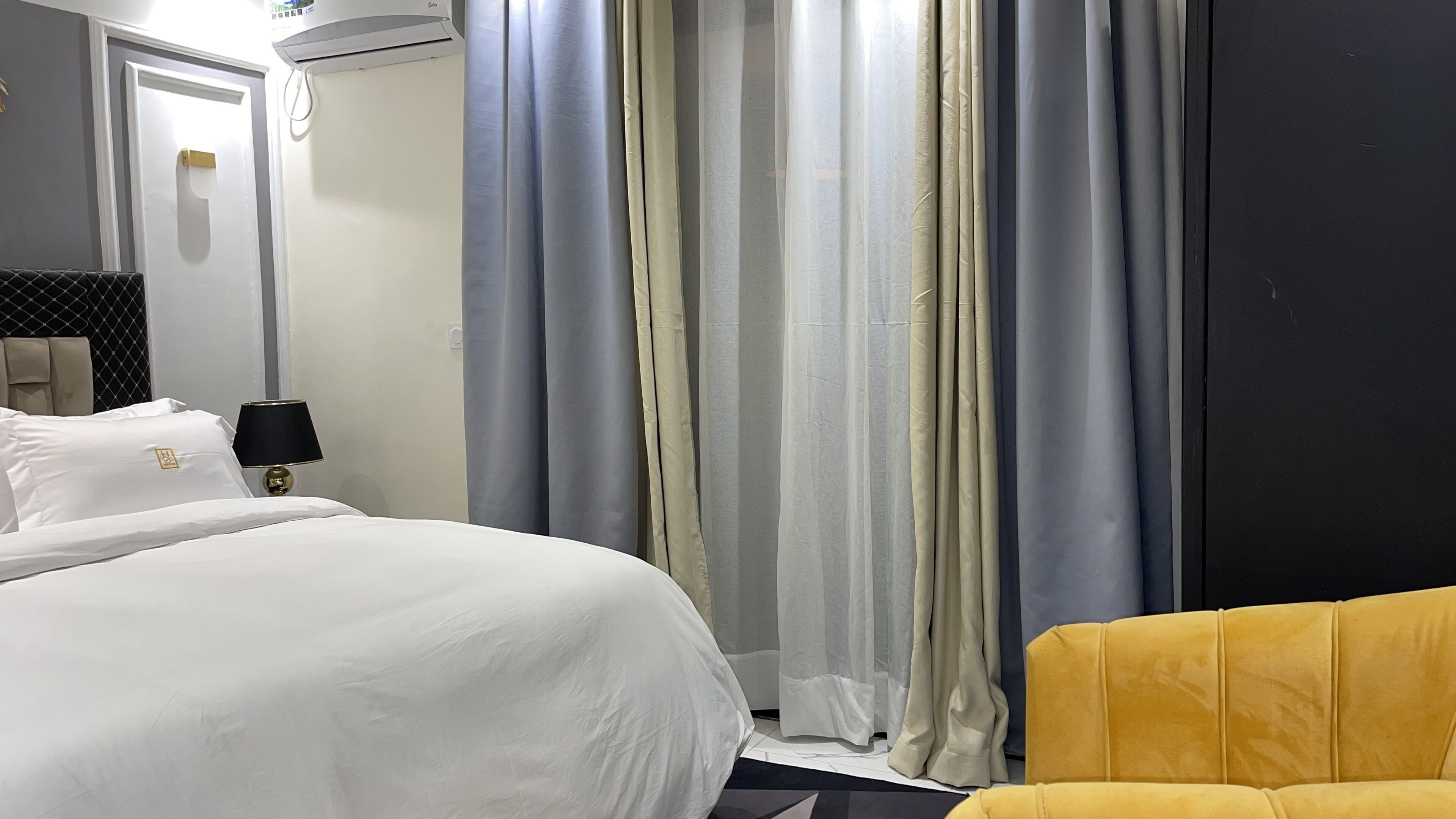 A hotel room with a bed, a nightstand, a lamp, a chair, and a window with curtains.