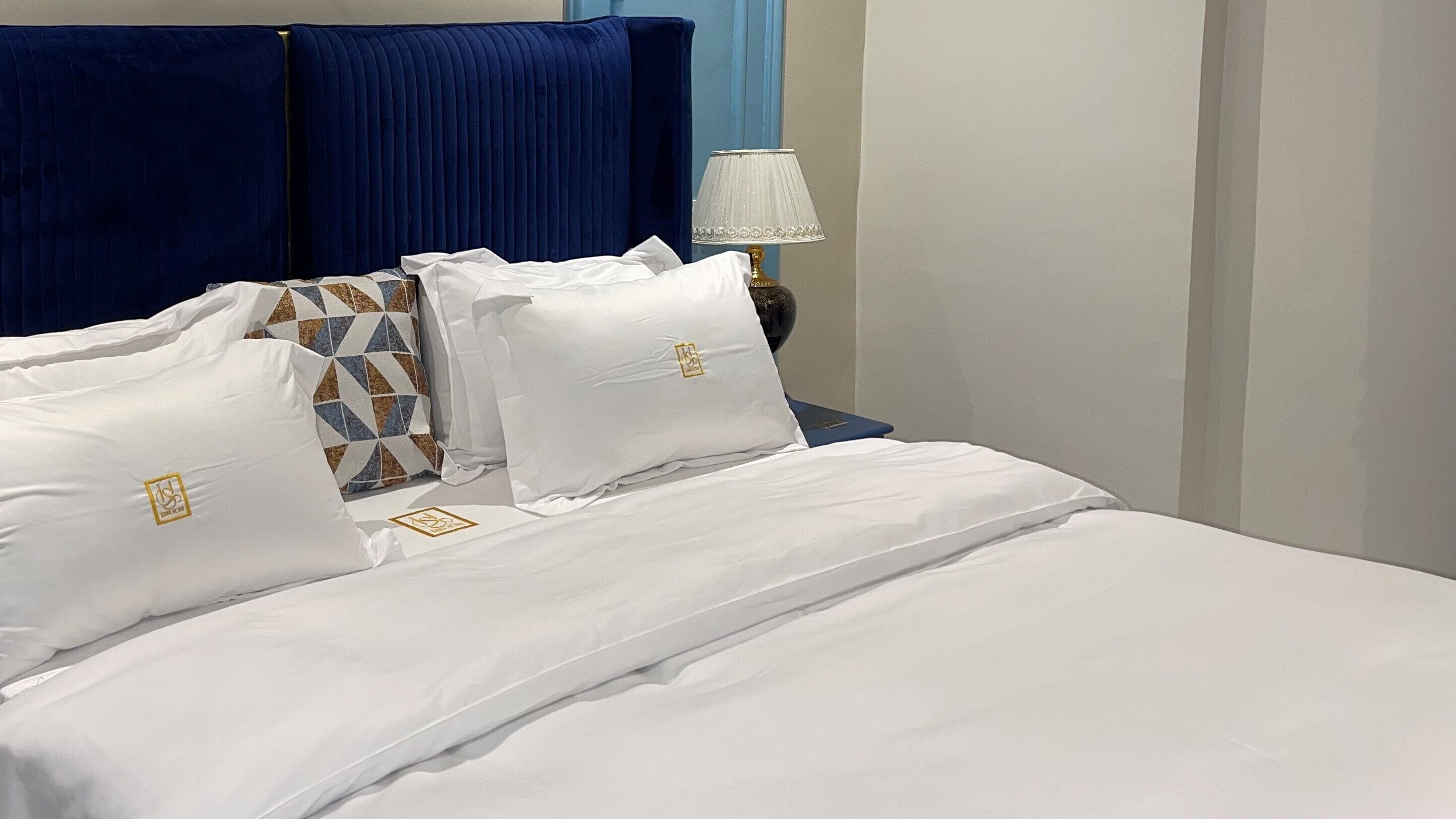 A neatly made bed with white linens and pillows, a blue headboard, and a bedside lamp.