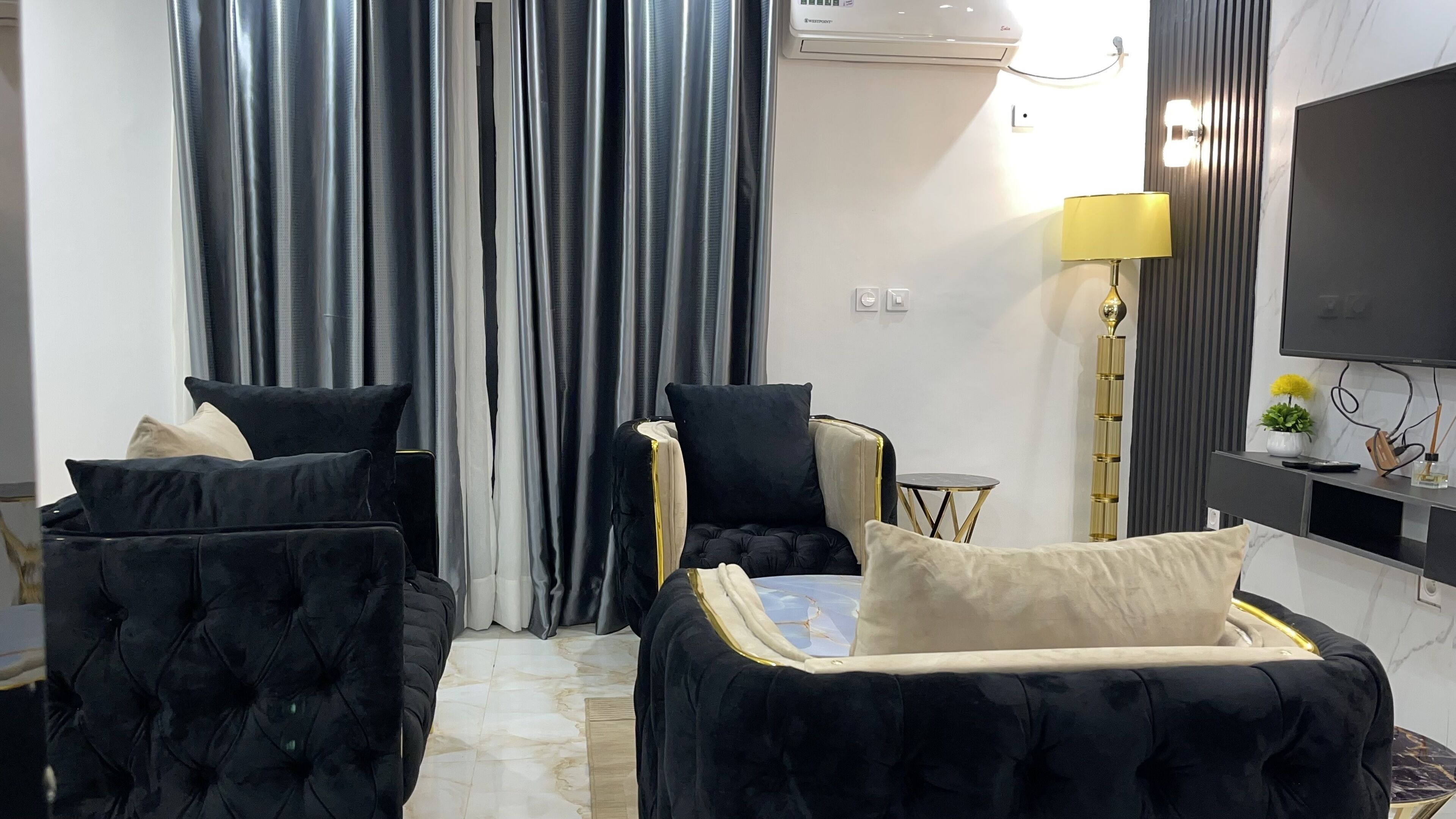 A modern hotel room with a sofa bed, a small round table, a lamp, and a TV mounted on the wall.