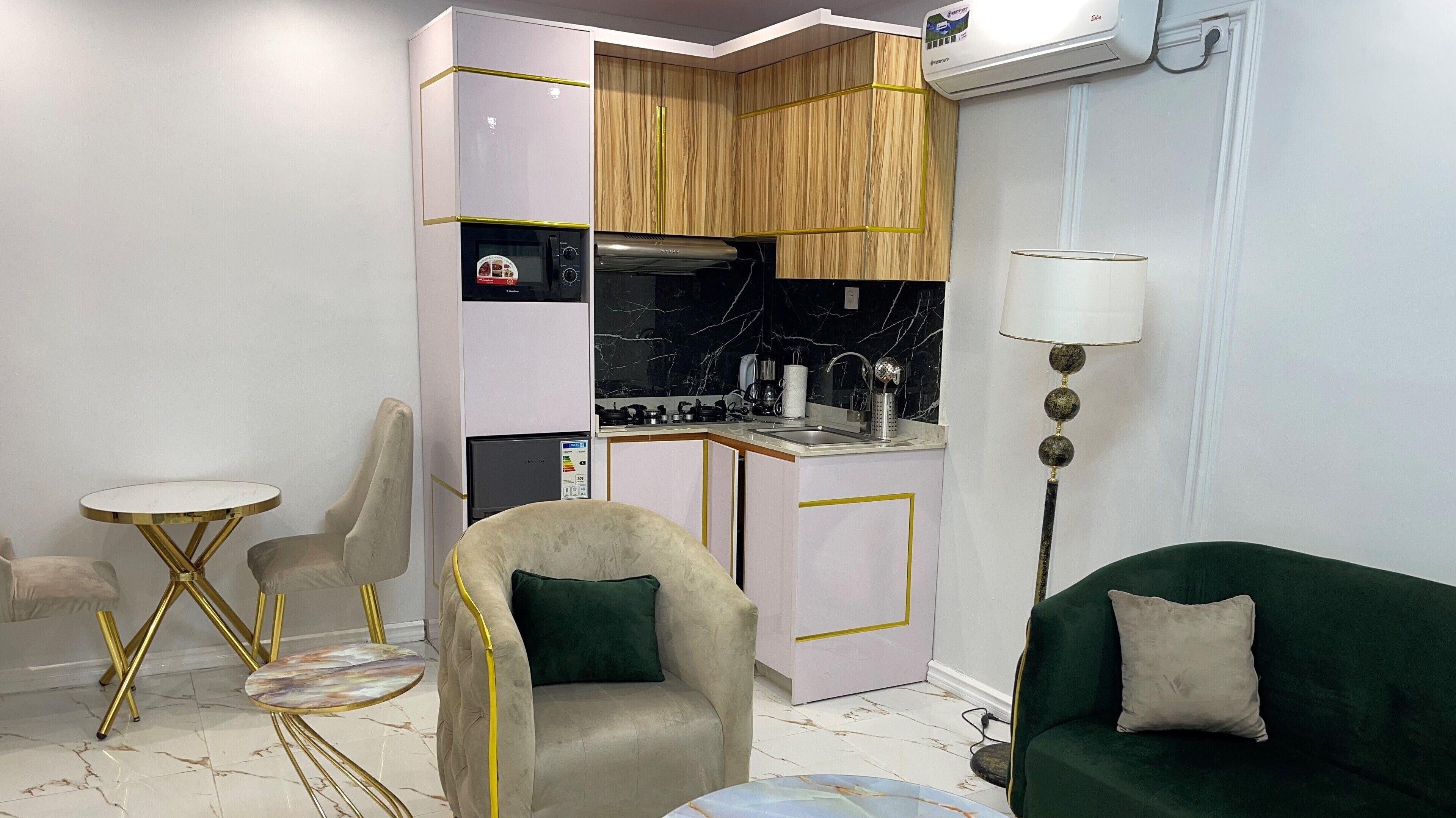 A compact living space with a kitchenette, a round gold-trimmed table, a beige armchair, and a green sofa.