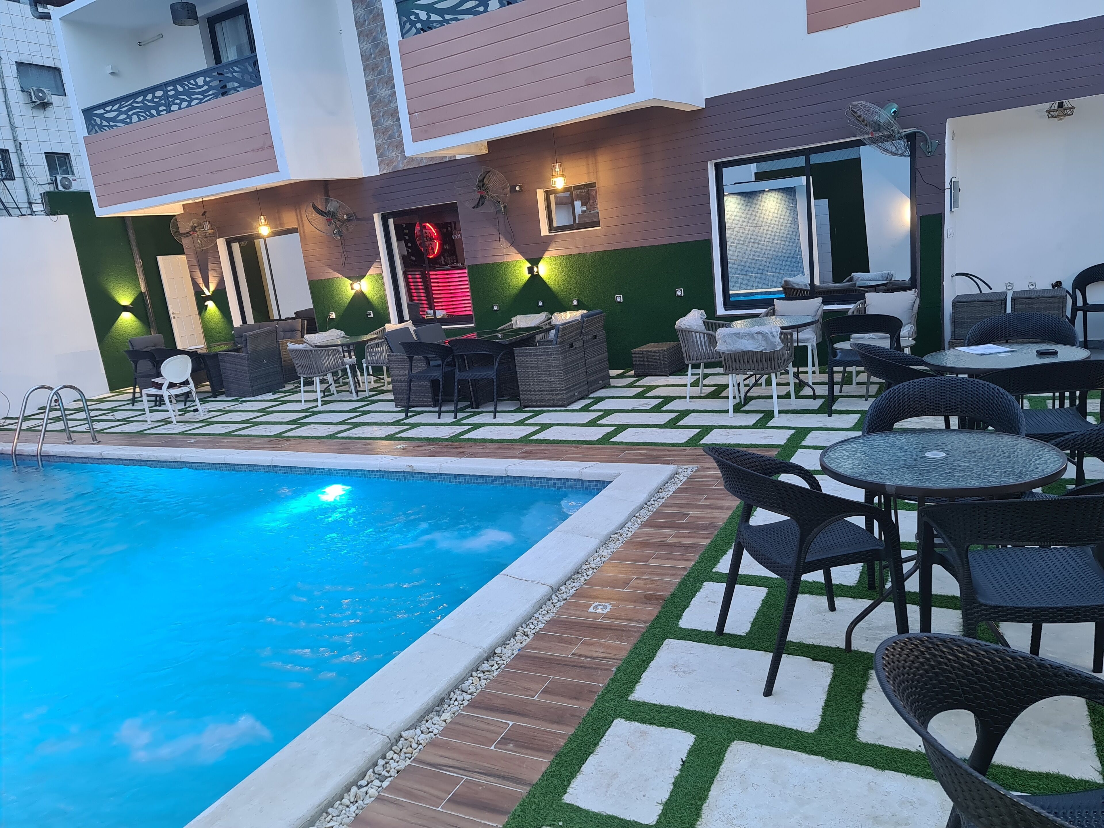 A pool area with a swimming pool, outdoor seating, and a building with a green and white facade.