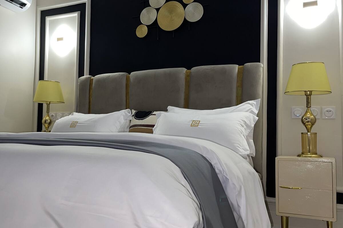 A neatly made bed with a grey and white duvet, two bedside lamps, and a wall-mounted decorative plate.
